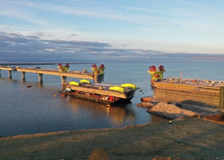 View of the Dronning Margrethe II Bridge under construction, with completed piers, bridge spans, and construction platforms positioned across the strait.
